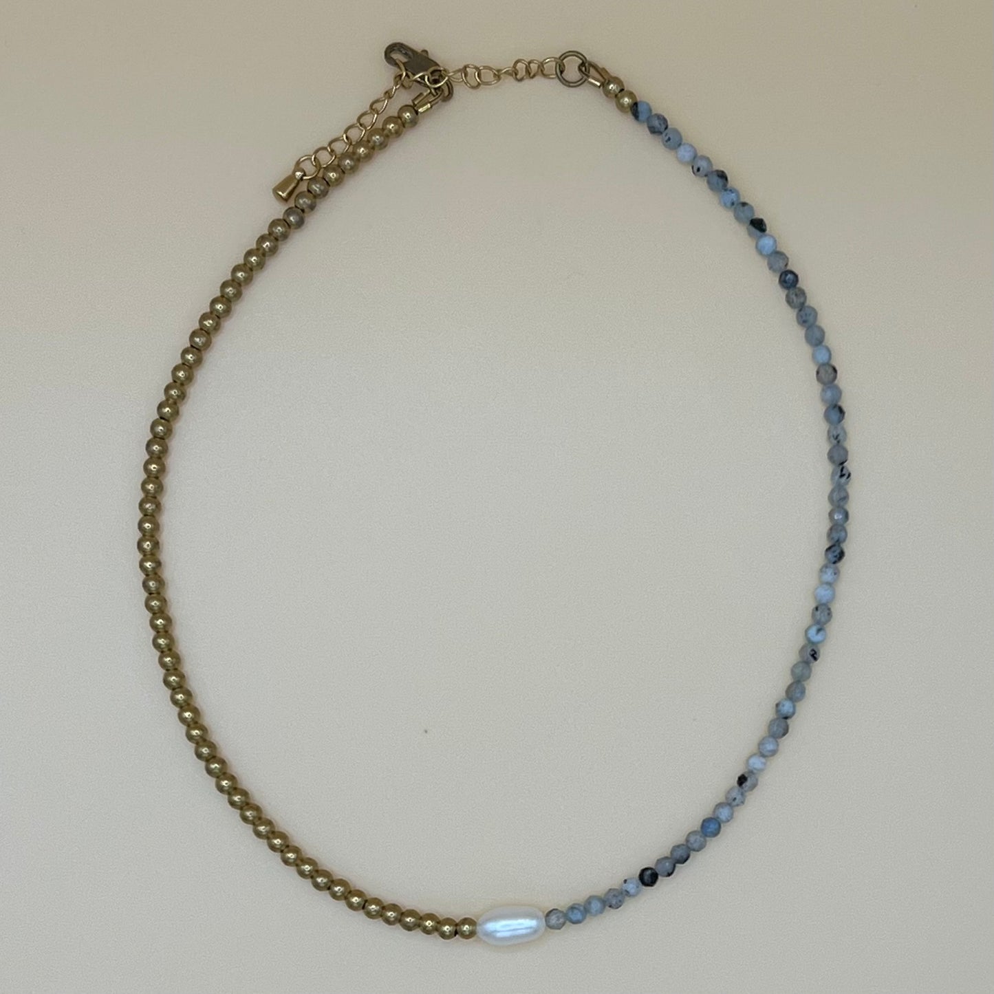 Close-up of handmade dainty pearl choker with aquamarine gemstone and brass beading, photographed on neutral background