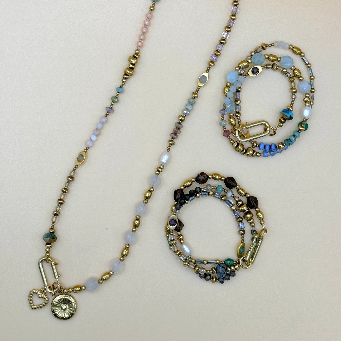 Flat lay of May & Moon’s Everything handmade jewelry collection, featuring layered beaded necklaces and wrap bracelets with pearls, gemstones, and gold accents.