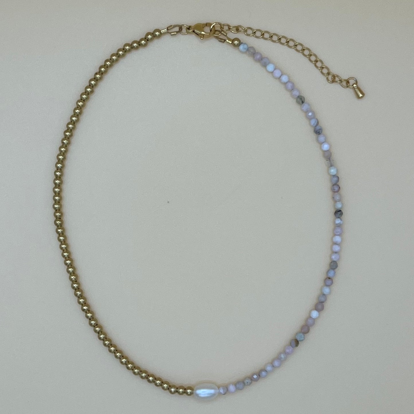 Flatlay of dainty pearl and gemstone choker necklace with gold and aquamarine beading, shown on neutral background