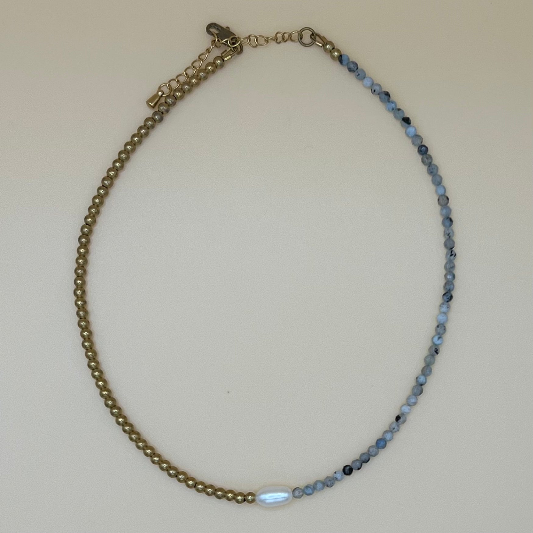 Close-up of handmade dainty pearl choker with aquamarine gemstone and brass beading, photographed on neutral background