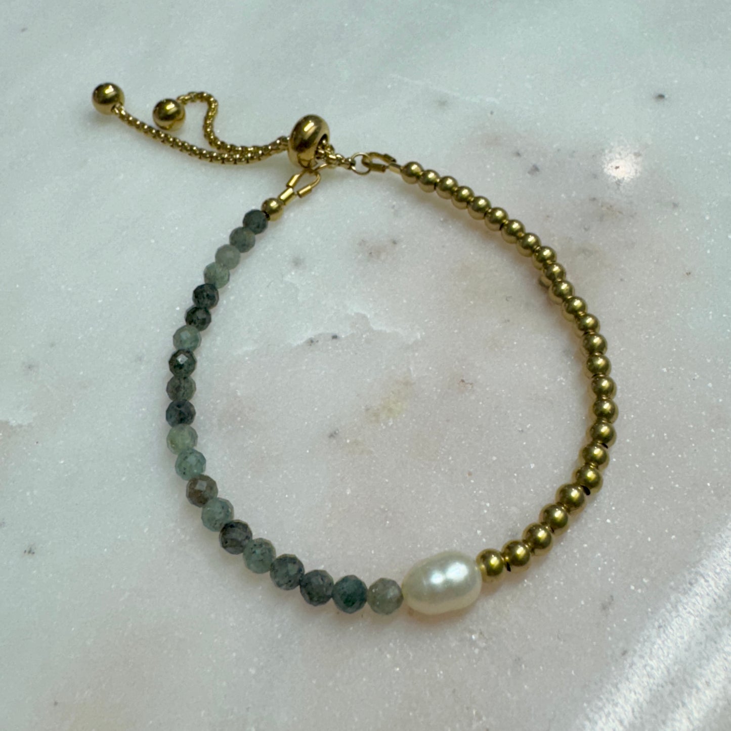 Lennon Bracelet with green-toned gemstones, freshwater pearl, and brass beads on marble — handmade and adjustable by May & Moon.