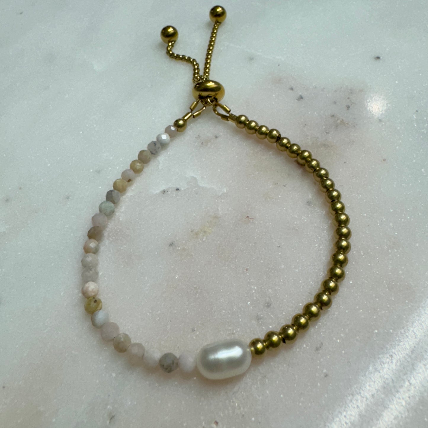 Lennon Bracelet by May & Moon shown on marble — handmade adjustable bracelet with freshwater pearl, brass beads, and speckled gemstones