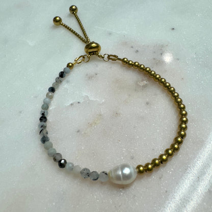 Lennon Bracelet by May & Moon shown on marble — handmade adjustable bracelet with freshwater pearl, brass beads, and speckled gemstones.