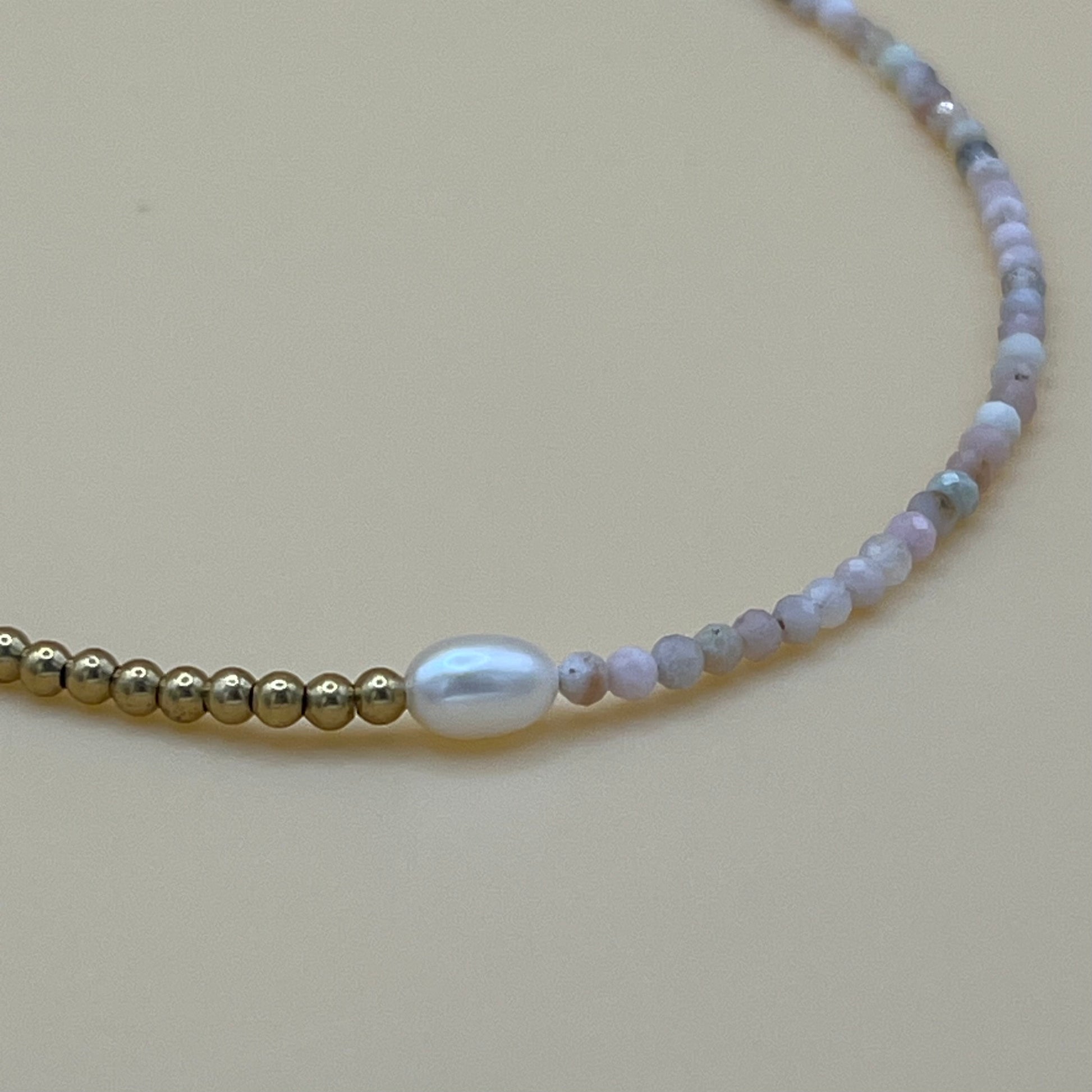 Macro close-up of freshwater pearl and gemstone beaded choker necklace with brass accents on neutral background